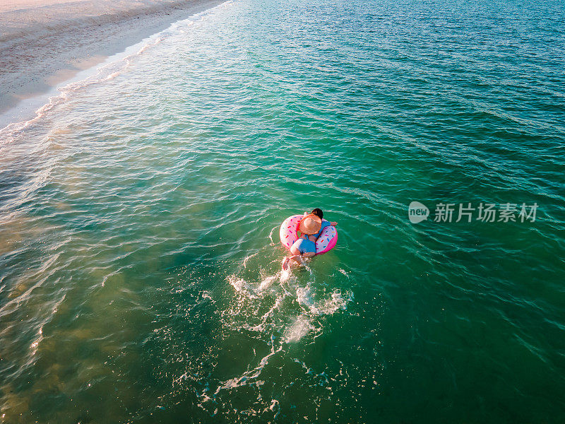 女人游泳和漂浮在海边的水与甜甜圈浮动鸟瞰图