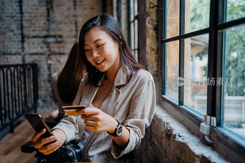 快乐的年轻亚洲女人网上购物使用智能手机和信用卡