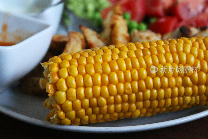 特写镜头:煮熟的玉米棒与薯条、豌豆和番茄片一起盛在盘子里