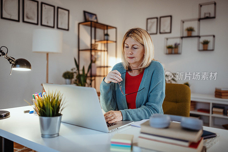 退休妇女在家用笔记本电脑工作，一边看着屏幕一边思考