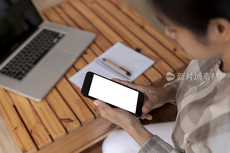 俯视图女性手握智能手机与空白白屏幕。女人的手在工作空间，近距离的手拿着智能手机空白屏幕在咖啡馆的文字和内容