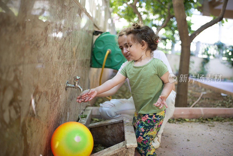 母亲和女婴在花园水龙头旁玩水