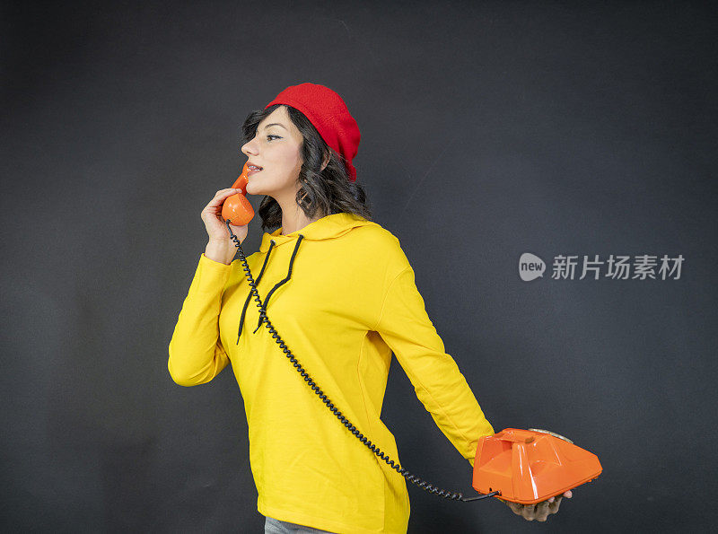 一个女人在老式橙色电话上拨打电话号码。漂亮的金发女人在用老式电话