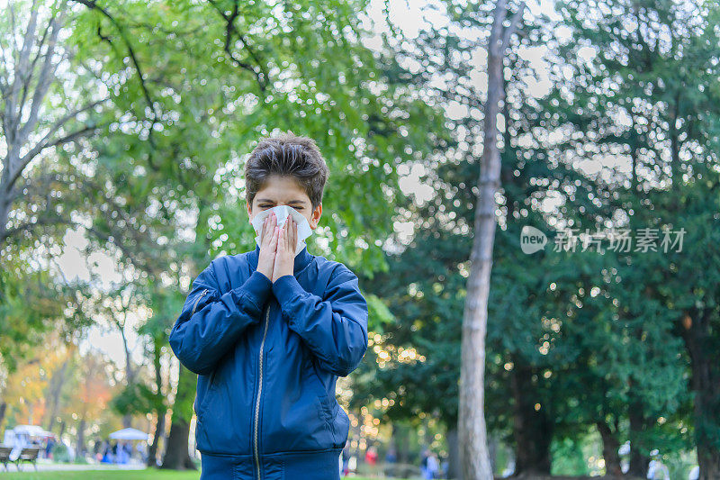 患流感的小男孩在公园里散步，用纸巾打喷嚏。