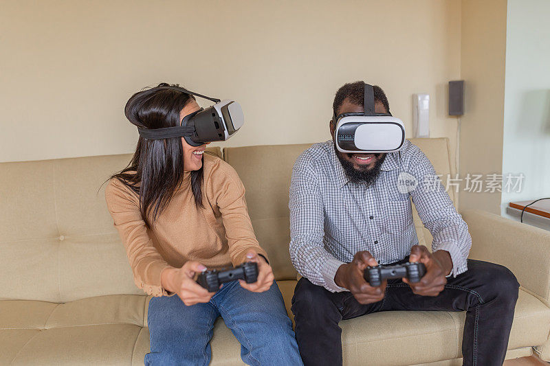一个快乐的非洲裔年轻人正在用虚拟现实模拟器和他可爱的华裔女友玩得开心。