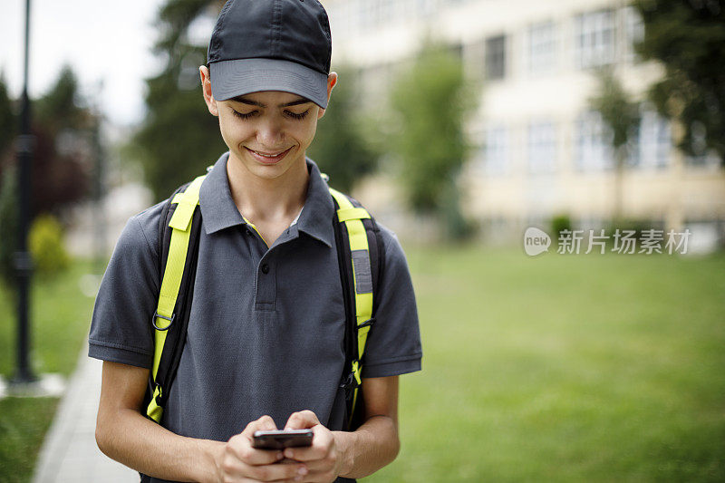 微笑的少年在学校前使用手机