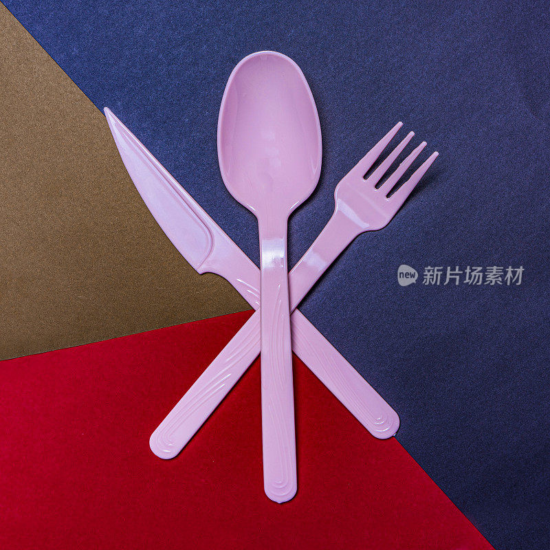 一次性粉红色塑料餐叉，餐刀，餐匙，蓝色，棕色，红色背景