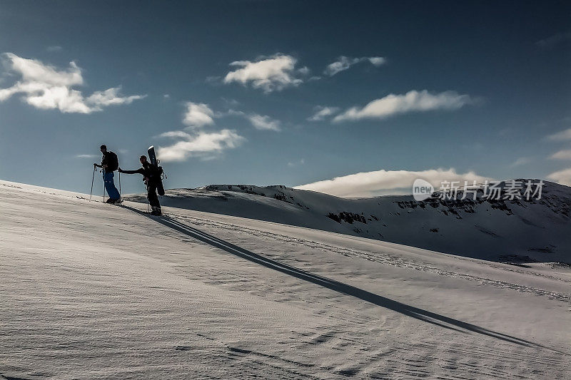 日落时分，在阳光的照耀下，一对登山运动员攀登一座雪山的剪影。