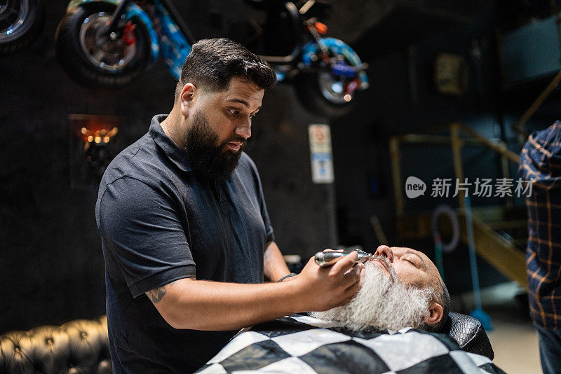 在理发店里，理发师正在修剪一个成熟男人的胡子