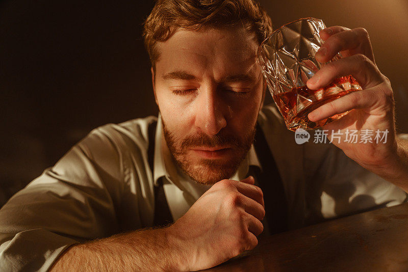 餐桌上一个喝着威士忌的醉汉的大气肖像。一个男人闭着眼睛的特写，一个男人的额头上放着一个装满威士忌的杯子。也许醉汉只是在伤心。