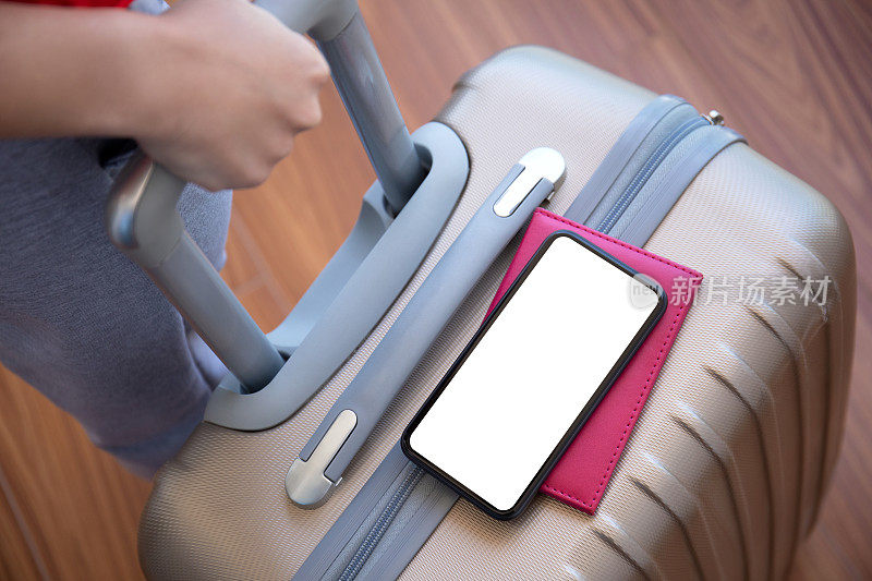 女性手拿行李箱，手机与机场隔离屏幕