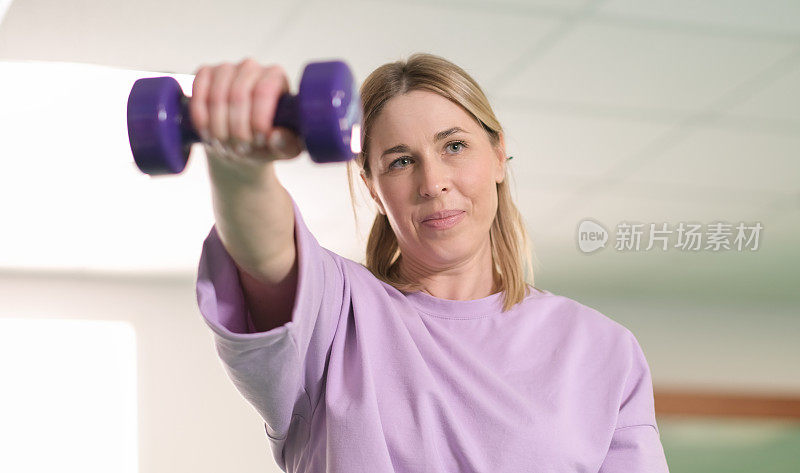 真正的女人在健身房用哑铃锻炼，独自训练，锻炼常规。举起哑铃。