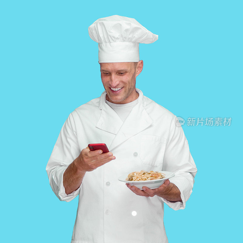 白种人年轻男厨师在蓝色背景下穿着裤子，用手机发短信