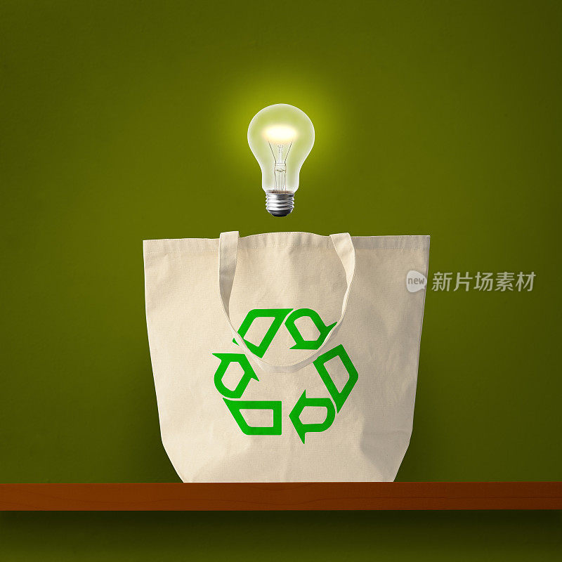 一个印有绿色回收标志的大手提袋，在半空中的架子上放着一个灯泡