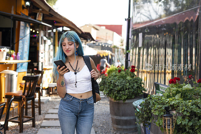 一位年轻的拉丁女子，蓝色头发，正坐在餐厅的桌子旁，用手机浏览菜单