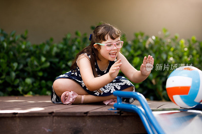 一个患有唐氏综合症的女孩微笑着在操场上把球扔过滑梯