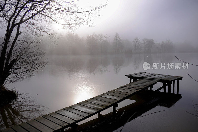 冬季雾蒙蒙的景观与老木栈桥通向森林湖泊