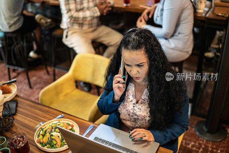 一名中年女商人在餐厅用手提电脑打电话