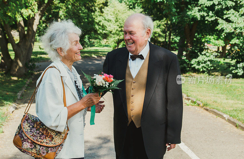 一对老夫妇在绿色的公园里散步。祖母和祖父在他们的金婚纪念日上。50年老人在一起的爱情故事。爷爷奶奶笑了。