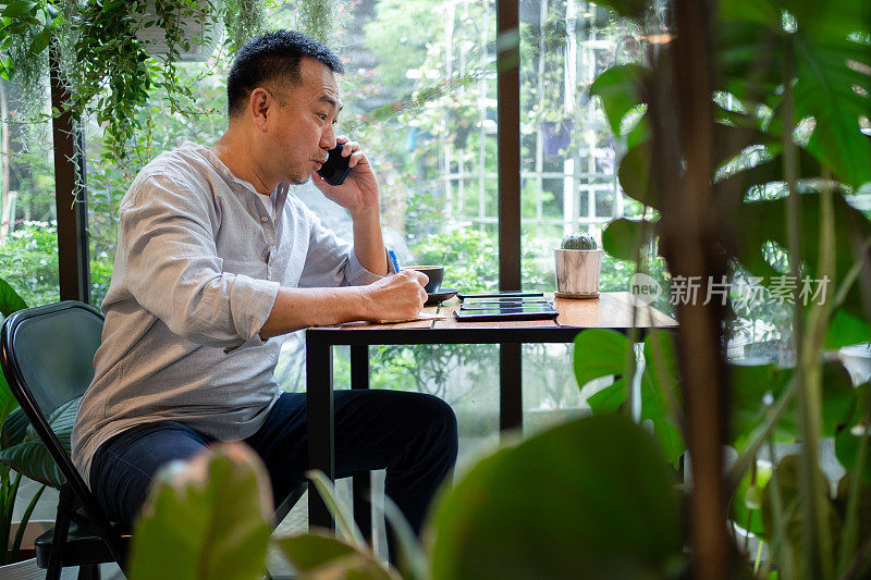 中年亚洲男子在咖啡馆打电话，惊讶地看着另一部手机