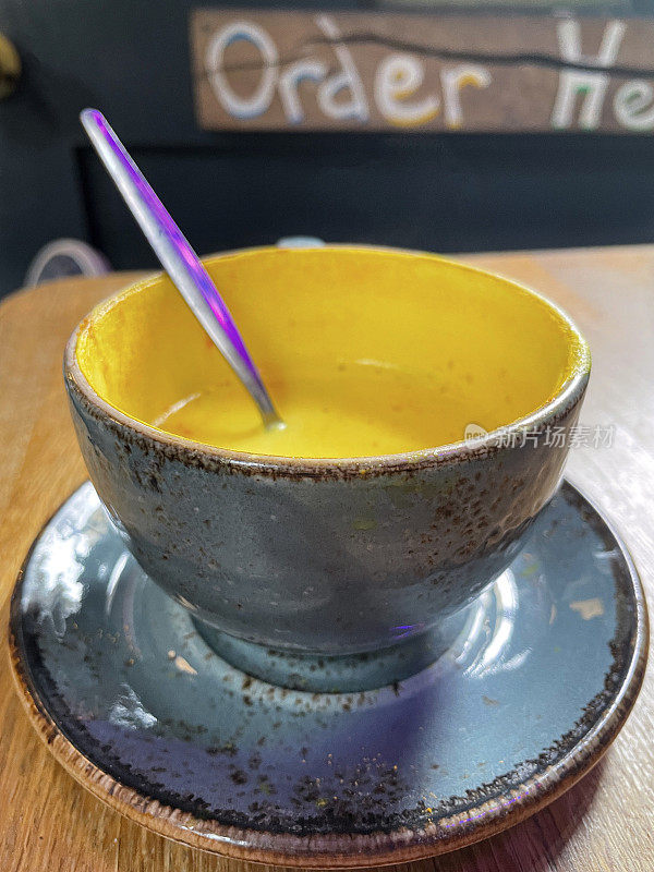 特写图像的咖啡桌场景与蓝色杯子在茶碟与勺子，姜黄拿铁咖啡，重点在前景