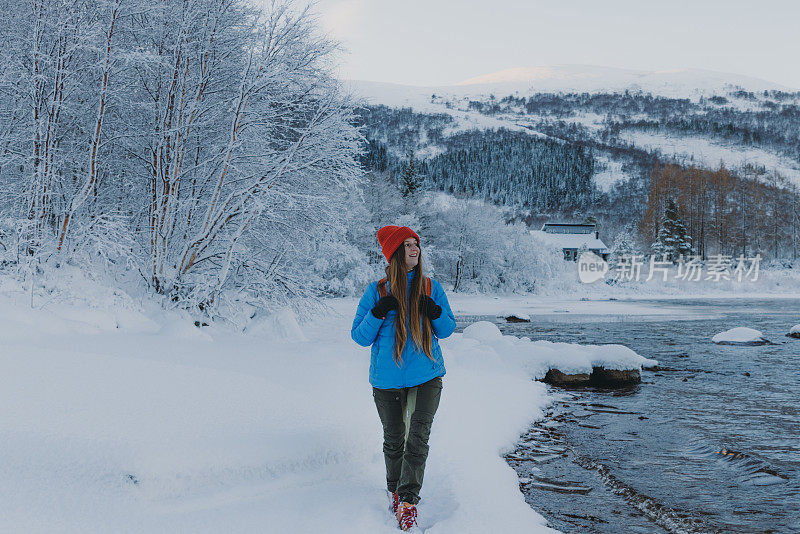 快乐的女人背着背包走在风景秀丽的冬季湖与山景日落在挪威