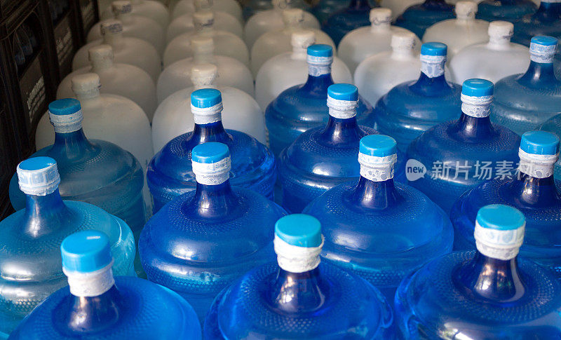 装有饮用水的蓝色水加仑和白色加仑已经用塑料密封密封在饮用水厂等待运送