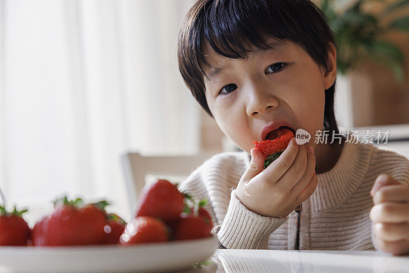 微笑的男孩在午餐时吃草莓。他在看摄像机。