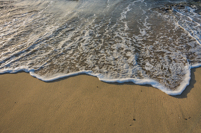 日出时，沙滩上的细沙上有白色泡沫的海浪