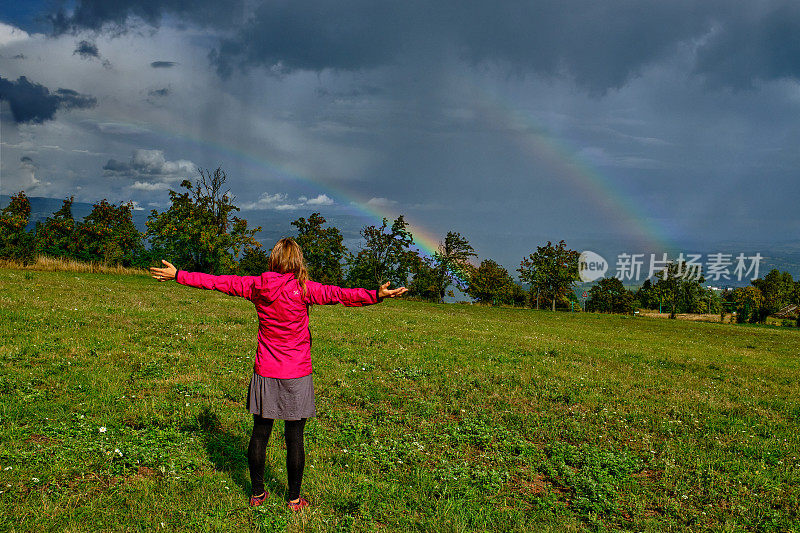 年轻女子看着彩虹上方的山谷在农村设置