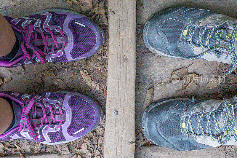 女士的登山鞋在男士的登山鞋前面，在一座自然的木桥上