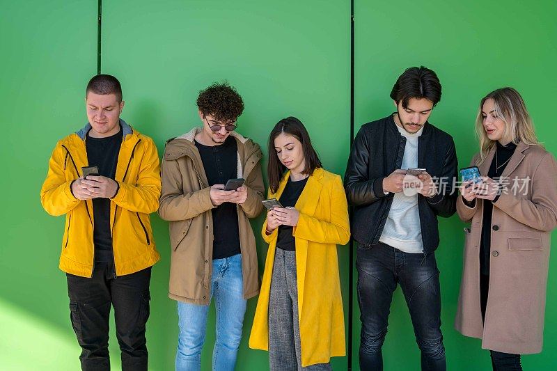 年轻人在户外使用智能手机——千禧一代享受社交媒体应用的新趋势——年轻人沉迷于科技——绿色背景