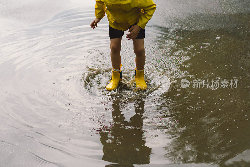 春天的一天，可爱的小男孩穿着雨衣和胶靴走过水坑