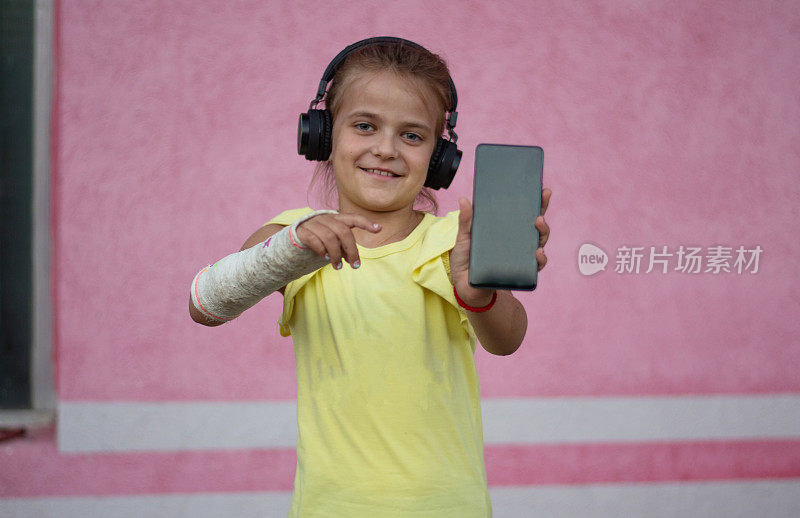 微笑的可爱小女孩的肖像，用智能手机打碎了耳机