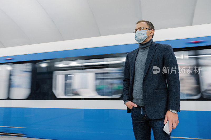 穿着蓝色西装、戴着口罩的通勤者站在地铁站里，身后是模糊的火车，描绘着疫情期间的城市生活