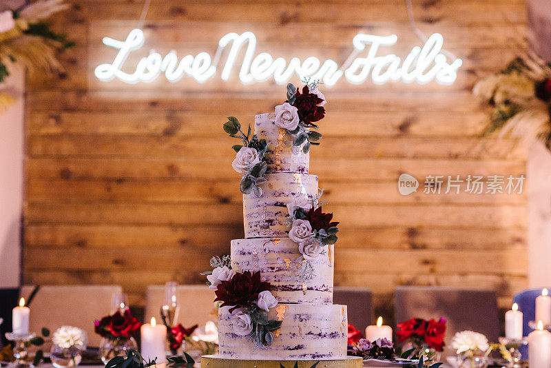 时尚分层白色和紫色，酒红色蛋糕与鲜花装饰和金色装饰。宴会上的糖果棒上的婚礼蛋糕。美味的婚宴。庆祝活动的概念。短信之爱永不失败。