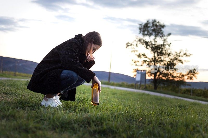 一个喝醉酒的年轻女子拿着一瓶啤酒朝汽车走去。