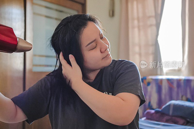 一位亚洲妇女在卧室用吹风机吹干头发