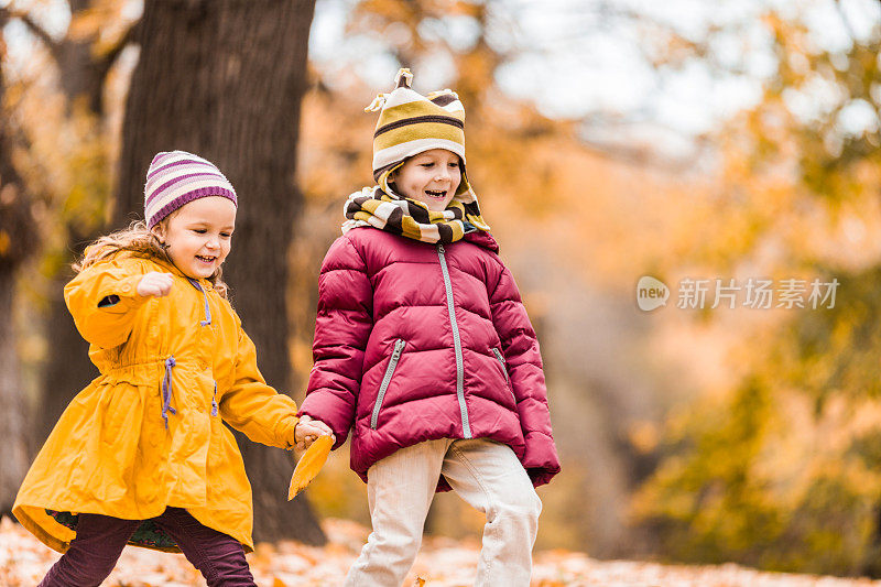 快乐的孩子们手牵着手在秋天的公园里散步。