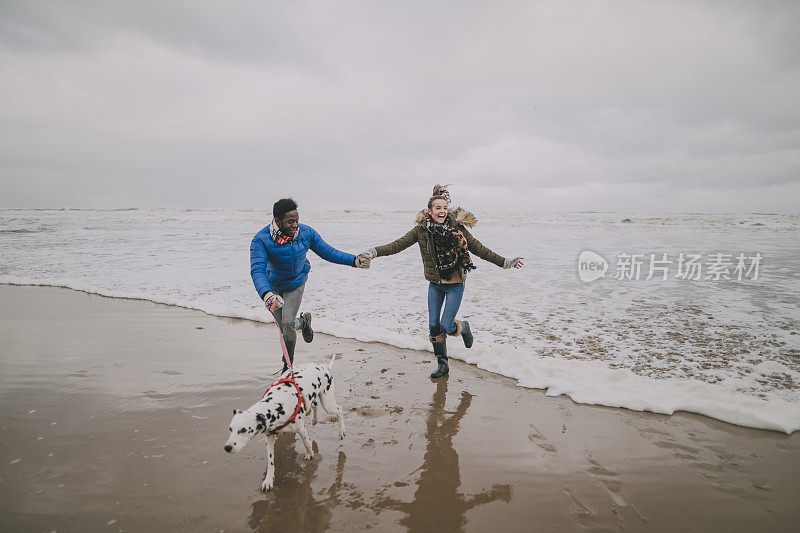 年轻夫妇在冬季海滩上躲避海浪