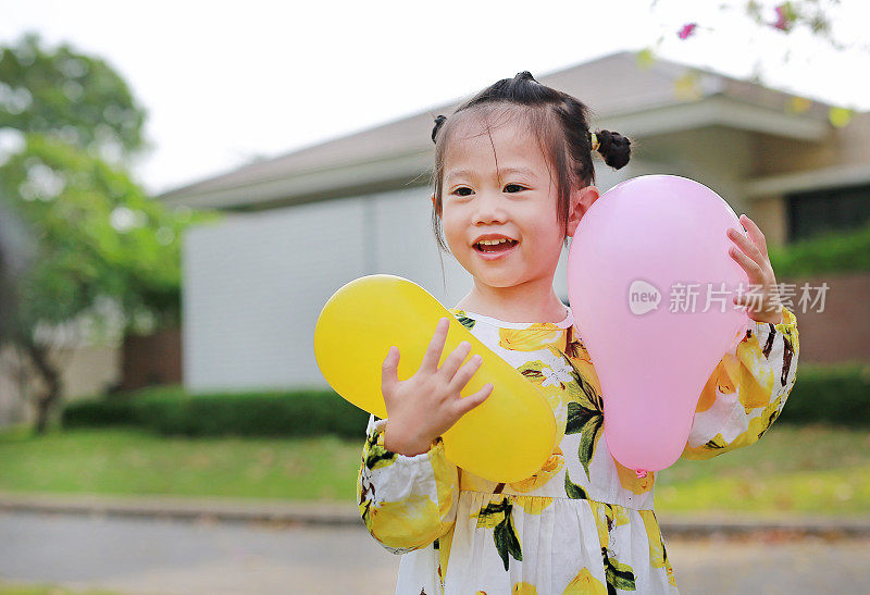 可爱的小女孩在公园里拿着气球，微笑着玩。