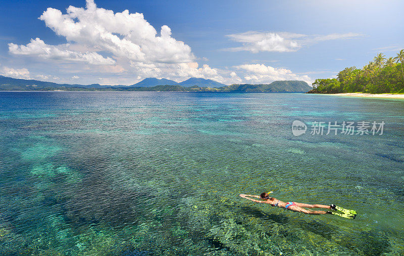女人在泳衣浮潜在珊瑚礁上面的热带海洋