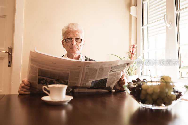 老年人在家里。老人喝着早上的咖啡，在家里看报纸