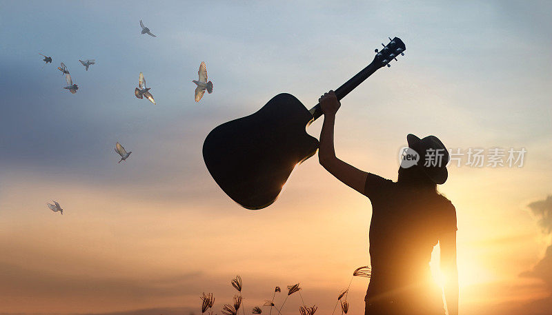 音乐家手持吉他与自由鸟的剪影在日落的自然背景