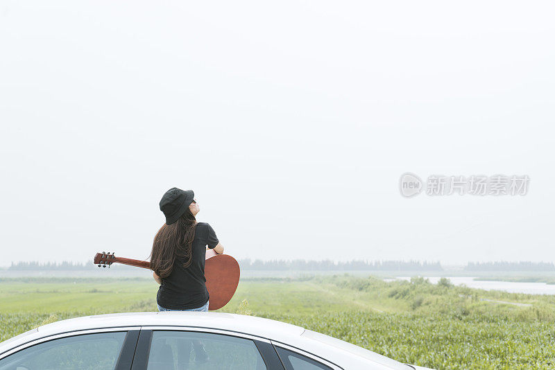 时尚女孩坐在车顶上，对着天空弹吉他
