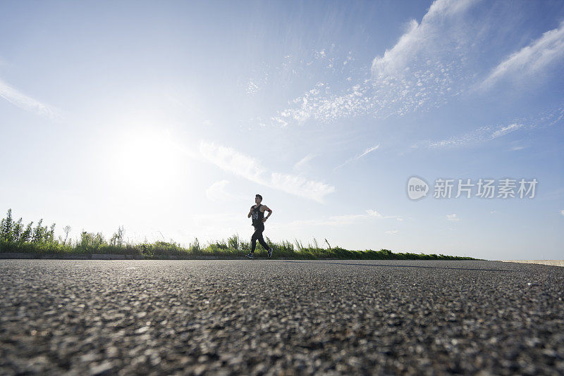 年轻的男运动员在柏油路上迎着天空奔跑