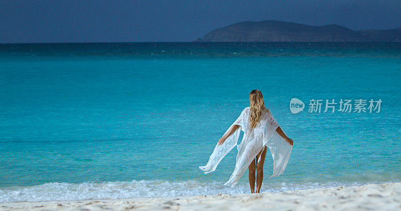 一个女人站在加勒比的热带海滩上，穿着飘逸的白色衣服