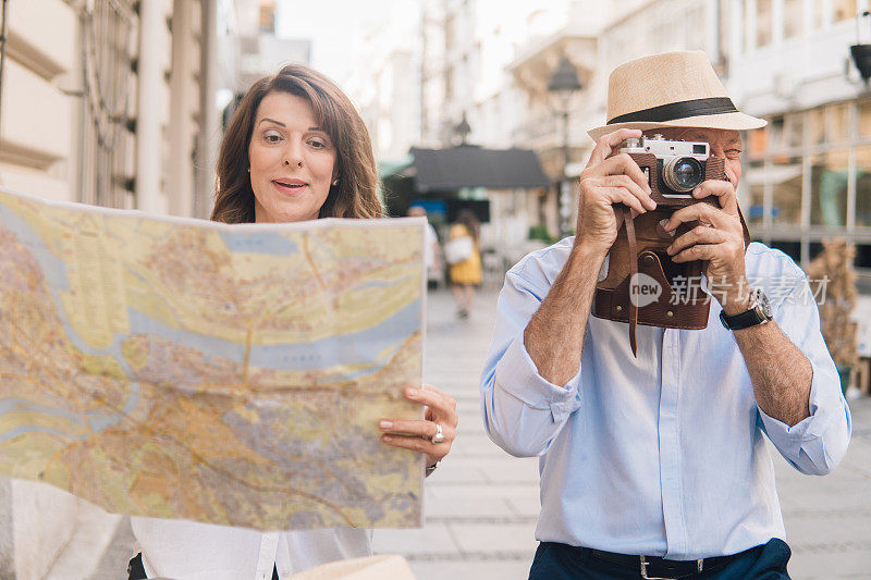 年长的女人在看地图，旁边的男人在拍照