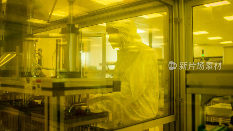 在制造设施拍摄的科学家在无菌防护服在工业3D打印机器上工作。生物技术的制造过程。用黄色滤光片从内部拍摄。