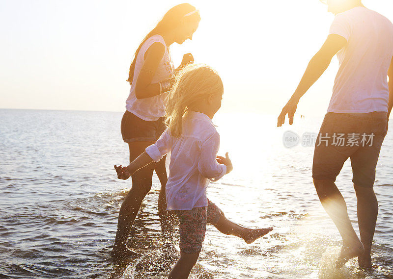 幸福的年轻的家庭在日落时在海滩上跑步